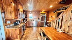 A wooden kitchen with granite countertops, a stainless steel refrigerator, and a dining area with a wooden table and chairs.