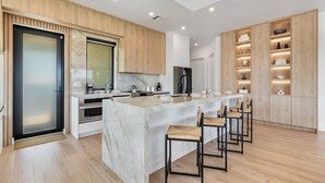 A modern kitchen with a central island, wooden cabinetry, and a built-in oven. - Upscale Canal-Front Escape w/ Private Pool, Dock & Water Views (Cudjoe Key)