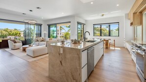 A modern kitchen with a marble island, large windows, and a dining area with a view. - Upscale Canal-Front Escape w/ Private Pool, Dock & Water Views (Cudjoe Key)