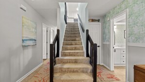 Un escalier recouvert de moquette, doté d’une main courante, qui mène à un palier avec une porte blanche.