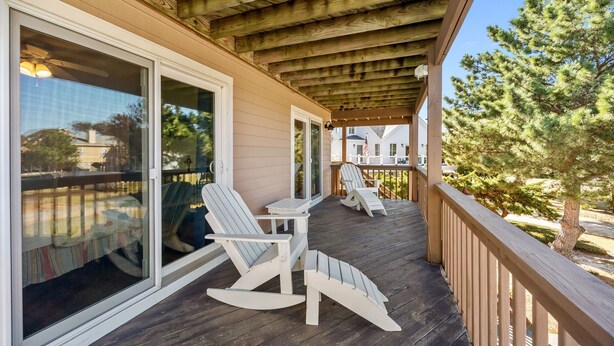 Une terrasse en bois avec des fauteuils à bascule et une table, donnant sur un quartier résidentiel avec des maisons et des arbres.