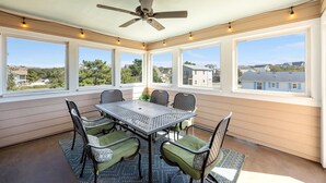Une terrasse couverte avec une table et des chaises, de grandes fenêtres et un ventilateur de plafond.