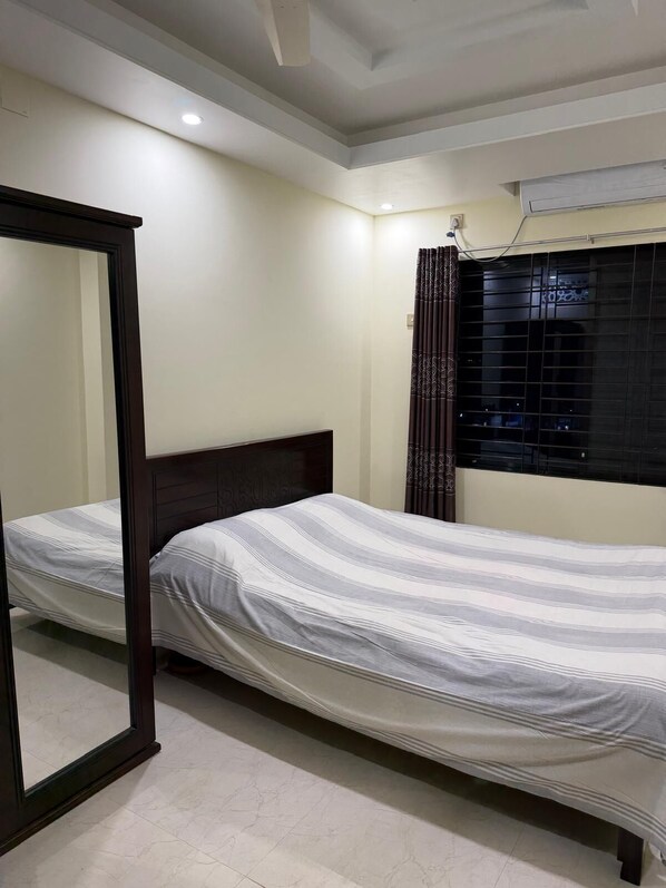 A bedroom with a bed, a mirror, a window with curtains, and an air conditioning unit.
