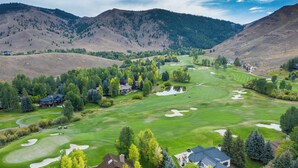 A golf course with multiple bunkers, a clubhouse, and residential buildings amidst a mountainous landscape. - 4BD Fairway Twelve Retreat + Resort Amenities (Sun Valley)