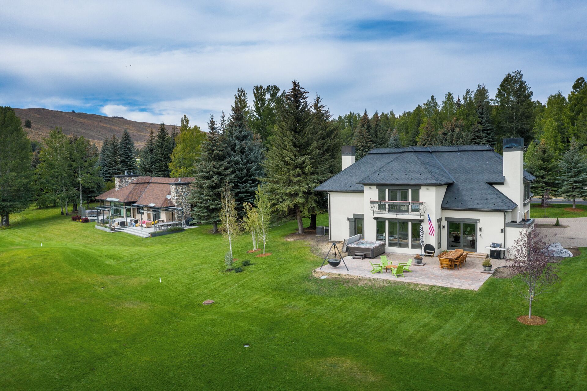Une maison moderne à deux étages dotée d’un grand patio, entourée d’une pelouse bien entretenue et d’une forêt dense.