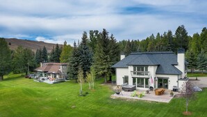 A modern two-story house with a large patio area, surrounded by a well-maintained lawn and dense forest. - 4BD Fairway Twelve Retreat + Resort Amenities (Sun Valley)
