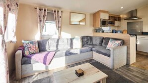 A modern living room with a grey sectional sofa, a wooden coffee table, and a kitchen area with wooden cabinets and a microwave. - Host and Stay 421 Wooler Park (Wooler)