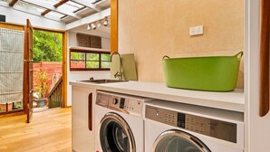 A compact kitchen with a washing machine, a sink, and a green pot on the countertop. - The Lilli Pad- A Tranquil Garden Stay (Lilli Pilli)