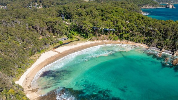 An aerial view of a coastal area with a sandy beach, clear turquoise waters, and dense forested hills. - The Lilli Pad- A Tranquil Garden Stay (Lilli Pilli)