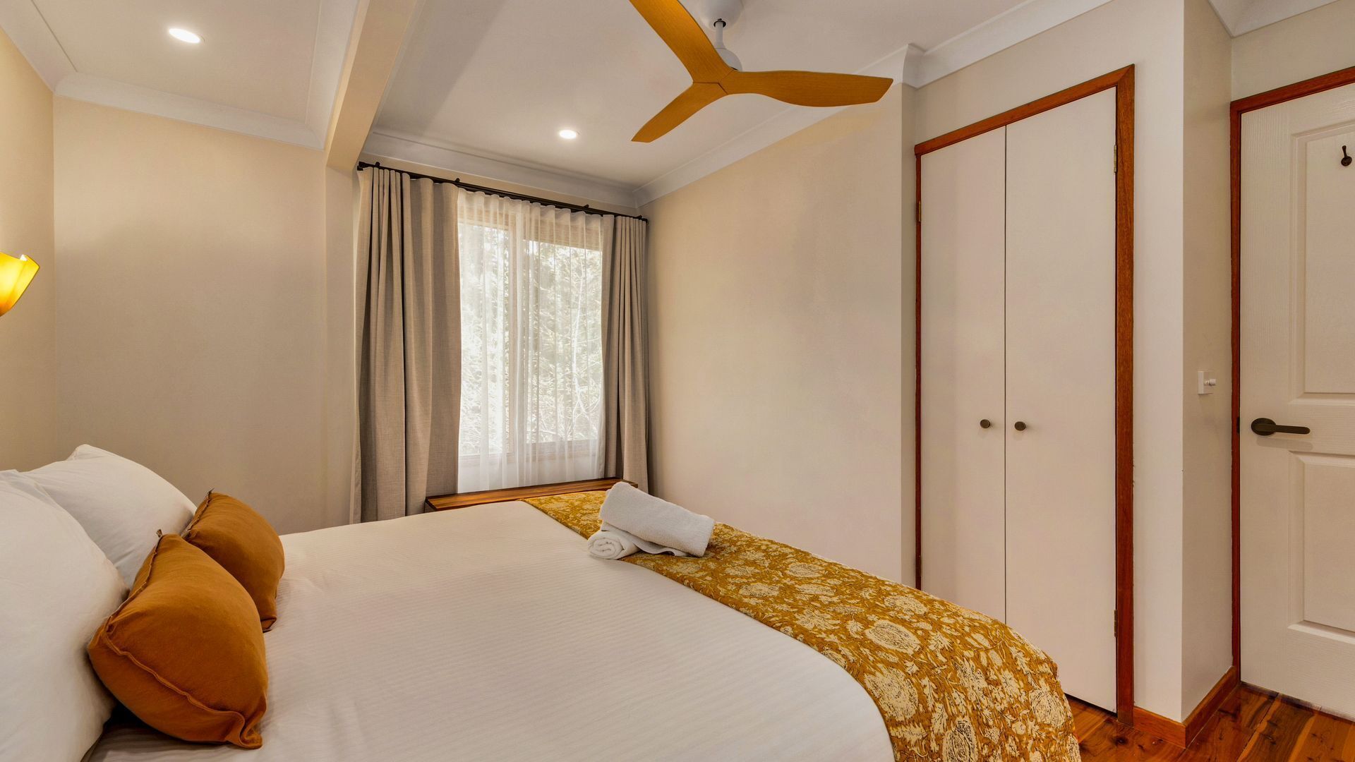 Quarto com cama, ventoinha no teto, janela com cortinas e guarda-roupa.