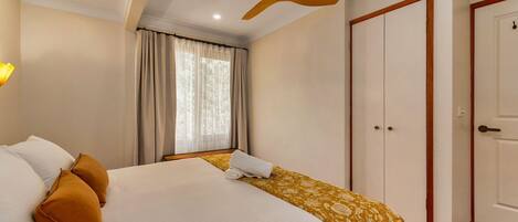 Quarto com cama, ventoinha no teto, janela com cortinas e guarda-roupa.