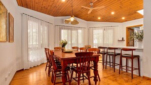 A dining area with a wooden table and chairs, large windows with sheer curtains, and a ceiling fan. - The Lilli Pad- A Tranquil Garden Stay (Lilli Pilli)