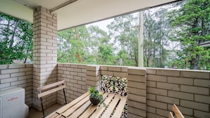 A balcony with a brick wall, a wooden bench, and a potted plant. - Your Calm Corner in Lane Cove North (Lane Cove North)