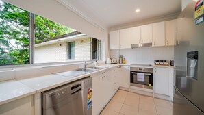 A modern kitchen with white cabinetry, a dishwasher, an oven, and a refrigerator. - Your Calm Corner in Lane Cove North (Lane Cove North)