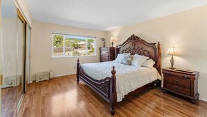 A bedroom with a wooden bed, a nightstand, a dresser, and a window with a view of a backyard. - Quiet and Spacious 4BR Goleta Home with a Big Yard and Near Beaches & UCSB (Goleta)
