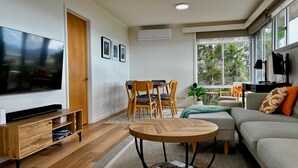 Un salon moderne doté d’un téléviseur à écran plat, de meubles en bois, d’une table basse ronde et d’un canapé agrémenté de coussins.