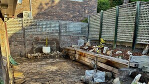 Un chemin de pierres mène à un espace jardin agrémenté de plantes et délimité par une clôture en bois.