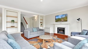 A modern living room with grey sofas, a fireplace, a television, and a staircase leading to another room.