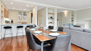 A modern dining area with a wooden table set for six, black chairs, and a grey sofa in the background.