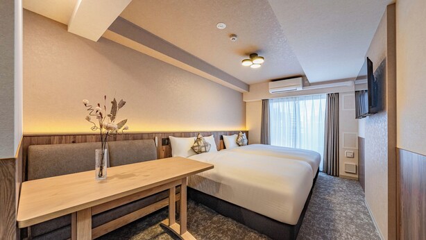 A hotel room with a bed, a sofa, a wooden table, and a vase with dried flowers. - Apartment Hotel 11 Nambaminami 5 (Osaka)