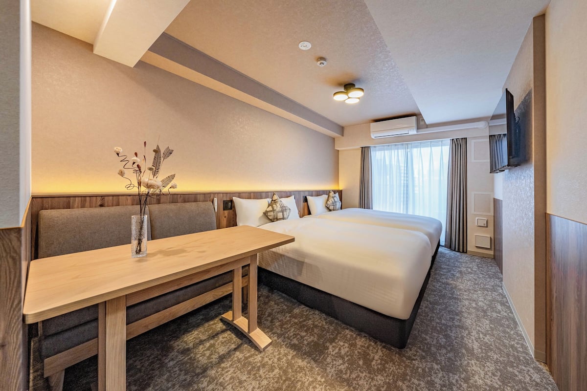A hotel room with a bed, a sofa, a wooden table, and a vase with dried flowers.