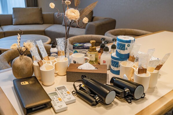 A hotel room with a neatly arranged table featuring toiletries, a vase with flowers, a remote control, and a smartphone. - Apartment Hotel 11 Nambaminami 5 (Osaka)