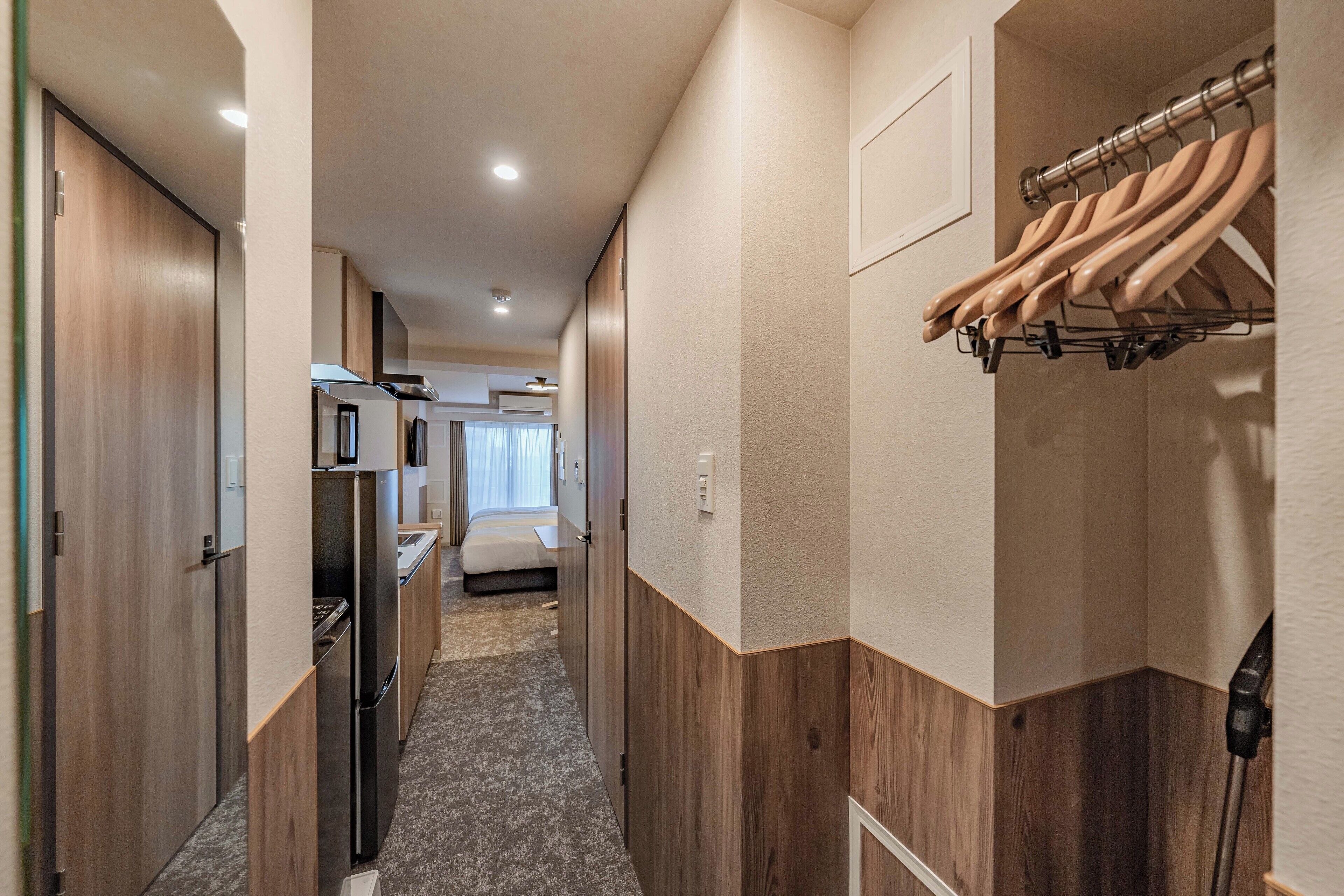 A narrow hallway with wooden walls, a kitchenette, and a bed in the background.