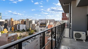 A balcony with a city view, a glass railing, and an air conditioning unit. - Apartment Hotel 11 Nambaminami 5 (Osaka)