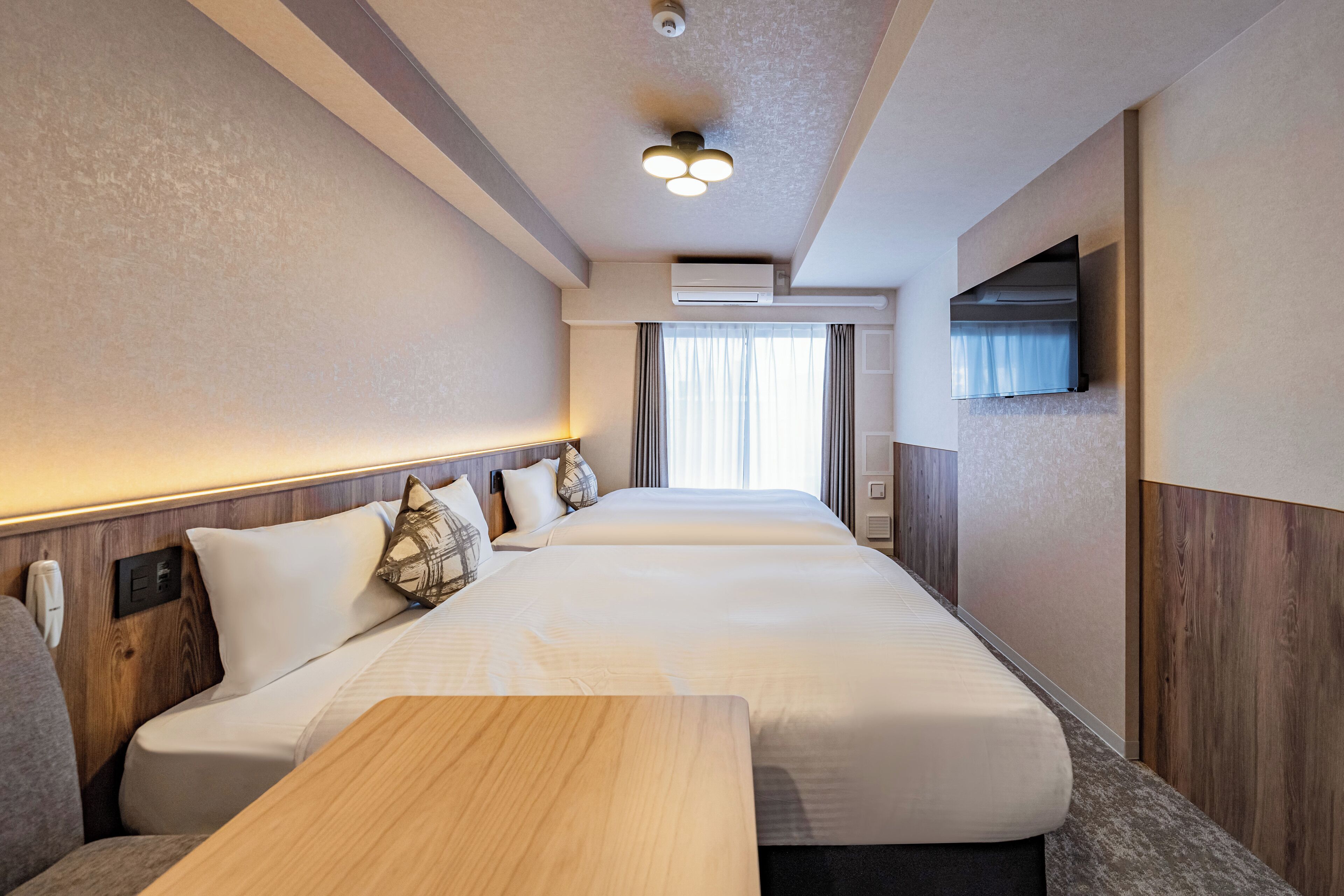Habitación de hotel con una cama grande, cabecera de madera, televisor de pantalla plana en la pared y una ventana con cortinas.