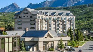 Un hotel de varios pisos con un diseño arquitectónico moderno, con balcones y ventanas grandes, con montañas de fondo.