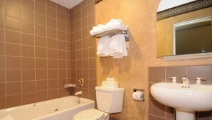 Un baño con bañera, inodoro y lavamanos. Toallas cuelgan de un perchero sobre el inodoro.