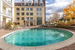 Ein Schwimmbecken mit Liegestühlen und ein Gebäude im Hintergrund mit mehreren Balkonen.