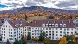 En stor byggnad med flera våningar och en symmetrisk fasad, troligen ett hotell eller ett bostadskomplex, omgiven av höstlövsverk och med ett bergigt landskap i bakgrunden.