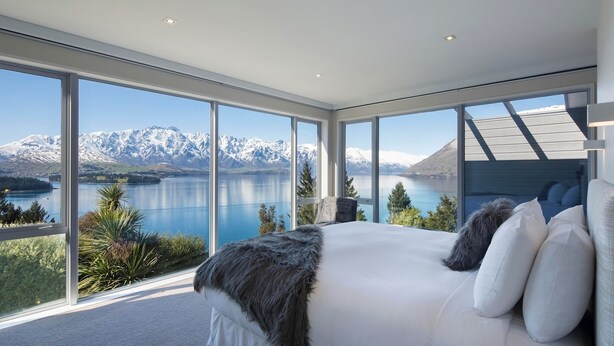 Una camera da letto con un letto grande, biancheria bianca e vista sulle montagne e un lago.