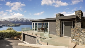 Ein modernes Haus mit einem Glasbalkon mit Blick auf einen See und Berge.