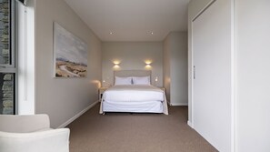 Ein Schlafzimmer mit Bett, Nachttischen, einem Sessel und einem Bild an der Wand sowie einer Tür.