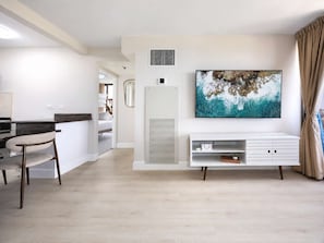 A modern living room with a large artwork, a white entertainment unit, and a dining area with a chair. - Waikiki Sunset 31st-fl with views, pool & parking (Honolulu)