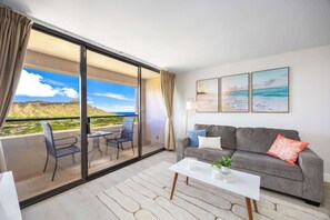 A modern living room with a balcony, a grey sofa, a white coffee table, and a view of the sea. - Waikiki Sunset 31st-fl with views, pool & parking (Honolulu)