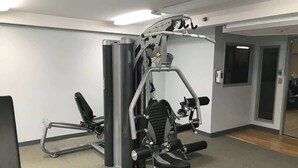 Een sportschool met trainingsapparatuur, een spiegel en een deur naar een andere ruimte.