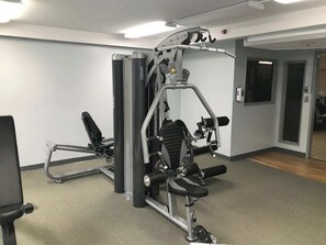 Ein Fitnessraum mit Trainingsgeräten, einem Spiegel und einer Tür zu einem weiteren Raum.