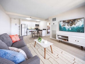 A modern living room with a grey sofa, a white coffee table, and a large painting on the wall. - Waikiki Sunset 31st-fl with views, pool & parking (Honolulu)
