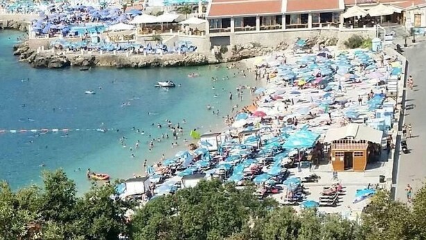 Ein belebter Strand mit vielen Sonnenschirmen und Menschen, die das Wasser genießen.