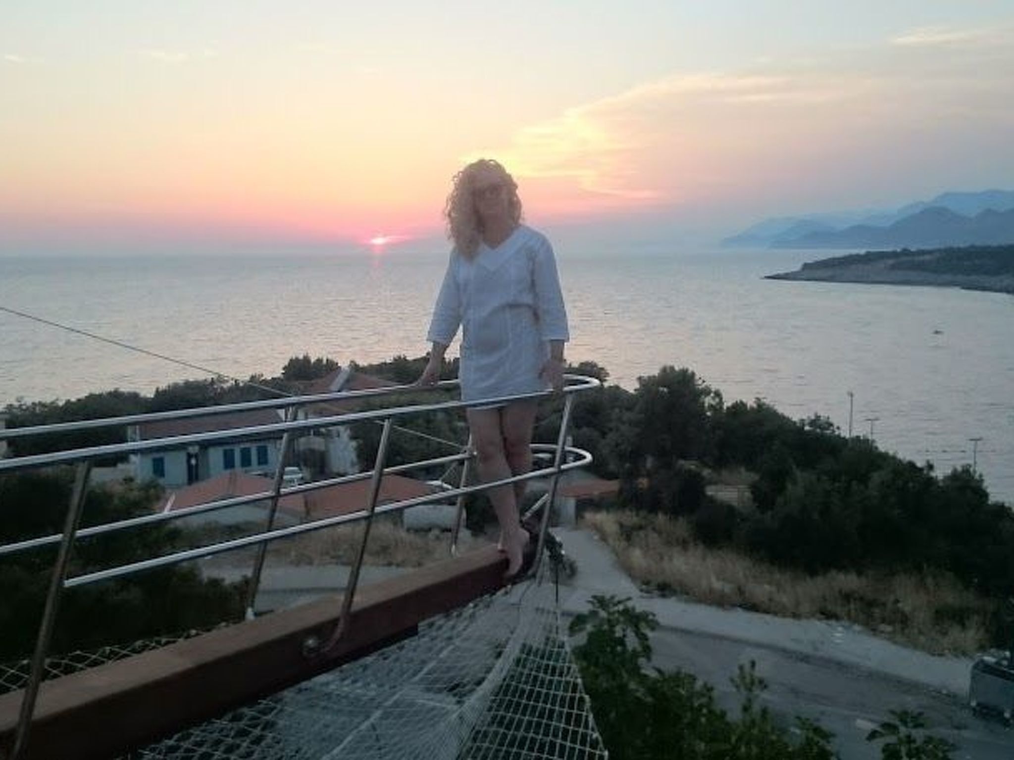 A person standing on a balcony overlooking a body of water during sunset.