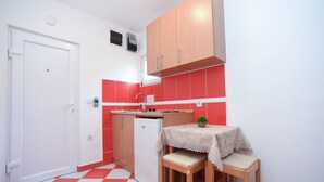 A compact kitchen with a red and white checkered floor, wooden cabinets, a small refrigerator, and a table with chairs. - Studio für 2 Personen by Interhome (Tivat)