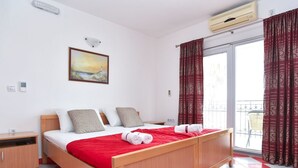 A hotel room with a wooden bed, a red and white checkered floor, a painting on the wall, and a window with patterned curtains. - Studio für 2 Personen by Interhome (Tivat)