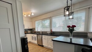Una cocina moderna con armarios blancos, encimera negra y una isla central. Hay un altavoz negro, un jarrón con flores y una lámpara colgante.