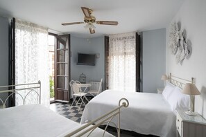 A hotel room with two beds, a ceiling fan, a TV, a small table with chairs, and a decorative wall piece. - Hostal Venecia (Granada)