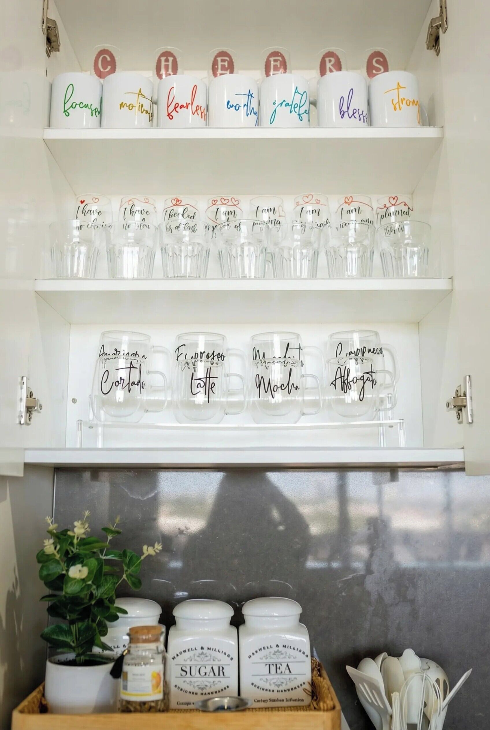 A kitchen shelf with jars labeled 'SUGAR' and 'TEA', a plant, and a tray with utensils.