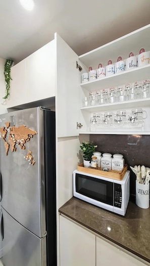 A kitchen with a stainless steel refrigerator, a microwave, and shelves with jars labeled with motivational phrases.