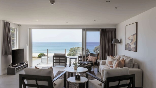 A modern living room with a large sliding glass door leading to a balcony with a view of the sea. - Sunrise & Sea views - Luxe downtown with 2 carpark (Mount Maunganui)